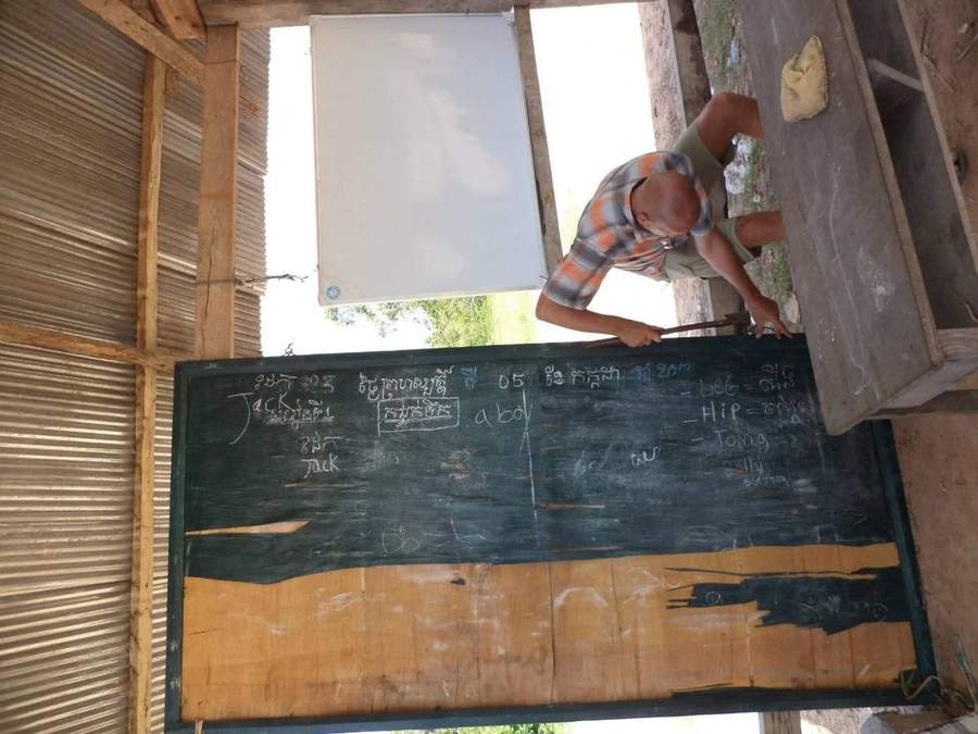 Volunteer writing English words on blackboard in open-air classroom