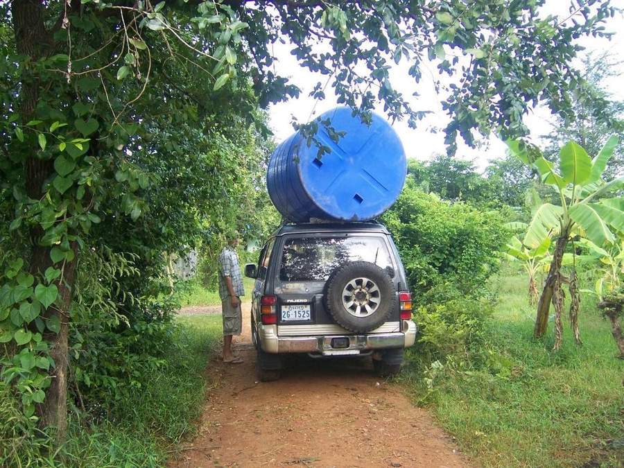 Large blue water tank strapped to roof of SUV on jungle road