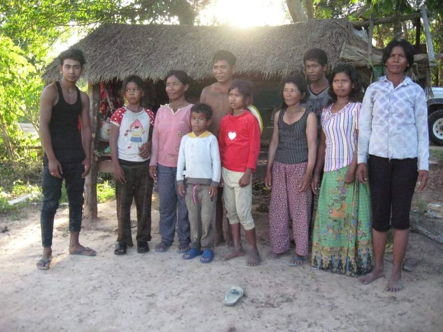 Cambodian family standing outside their thatched-roof home