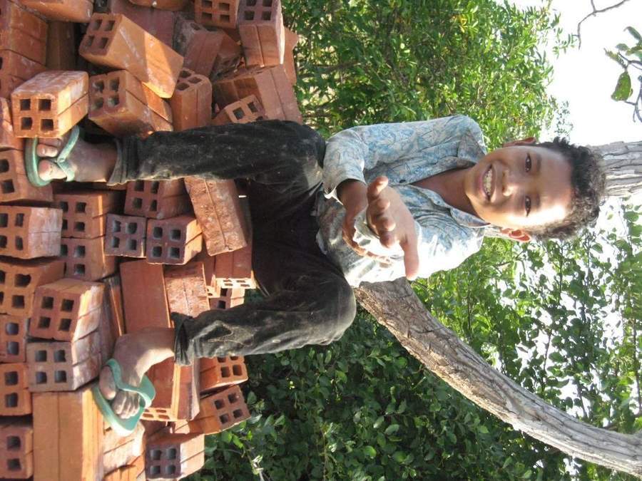 Young boy giving thumbs up sitting on pile of bricks