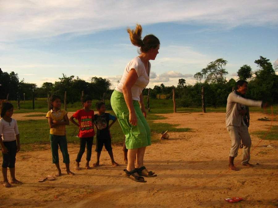 Volunteer and children playing jump rope on dirt field