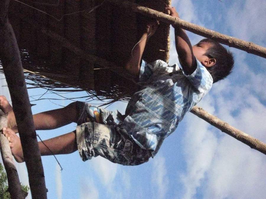 Boy climbing on wooden roof beams against blue sky