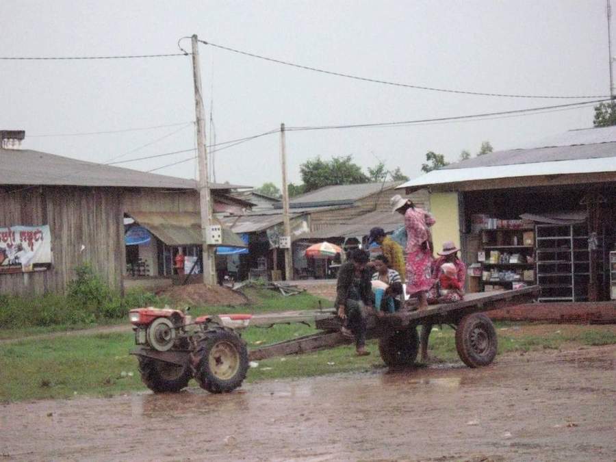 People riding on tractor-trailer through rainy village