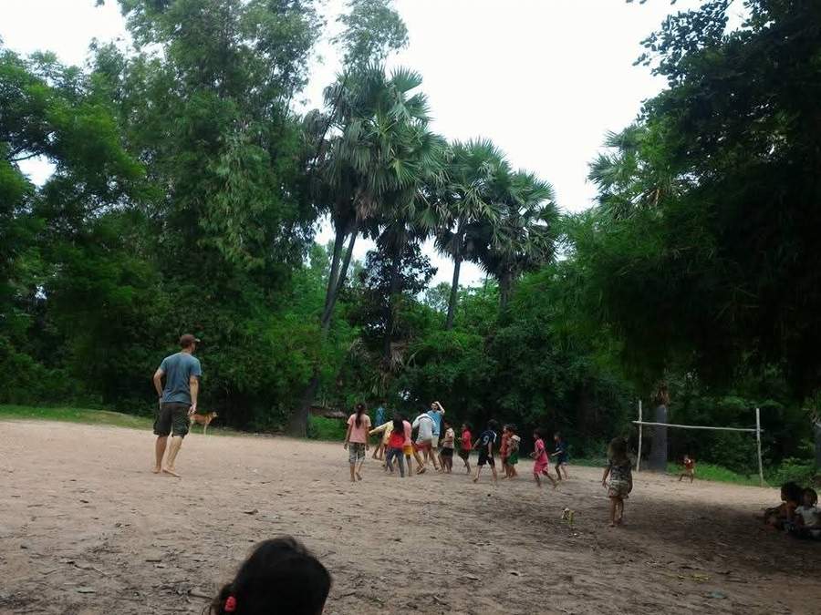 Volunteer playing with children on sandy clearing near forest