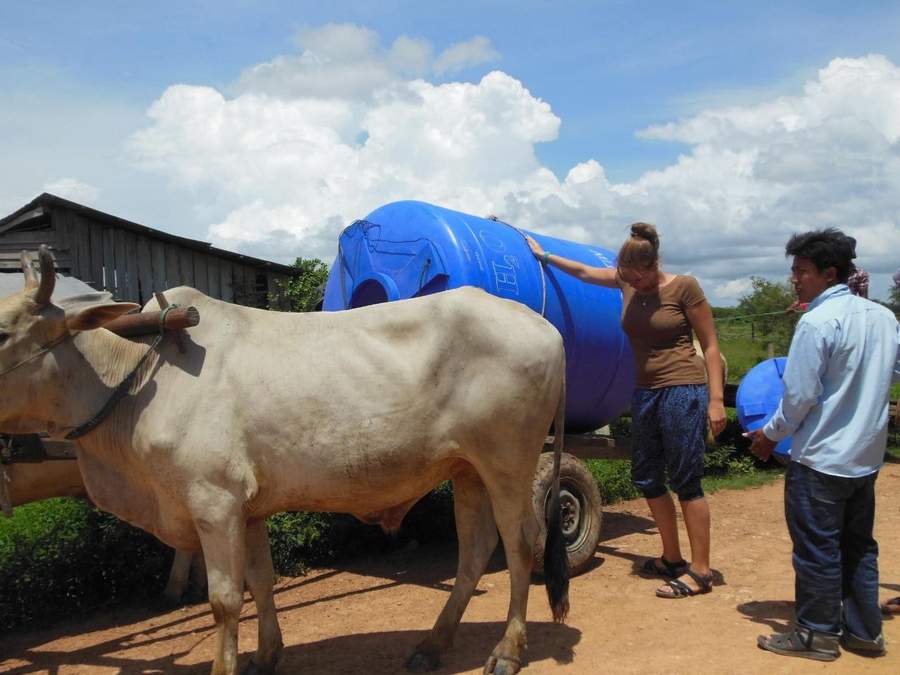 People loading blue water tank onto cart with oxen