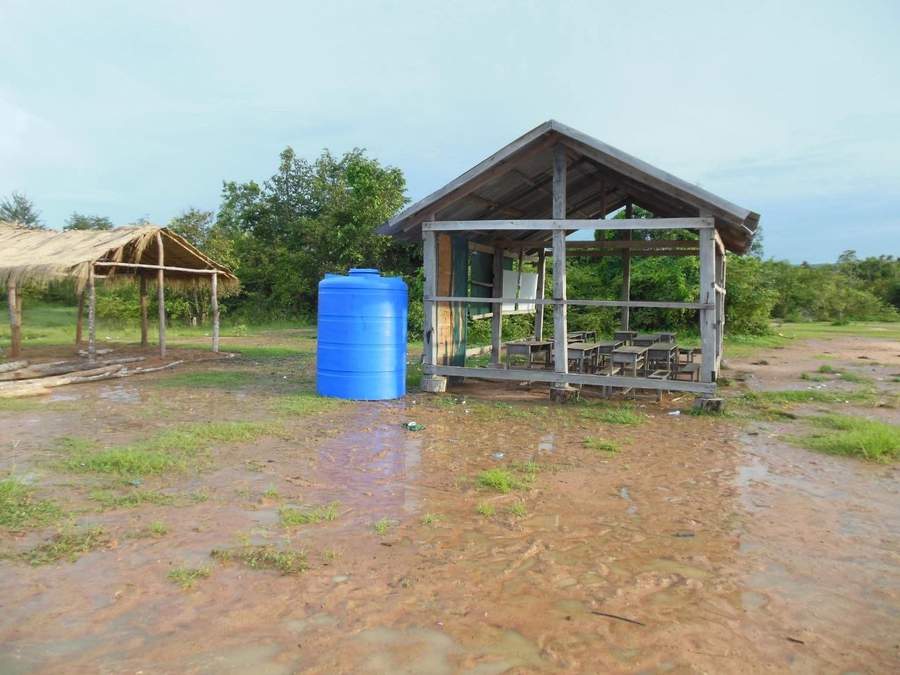 Blue water tank next to open-air school building in rain