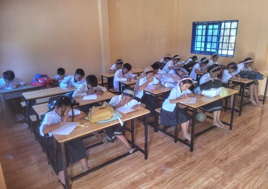 Students in uniforms writing at desks in classroom