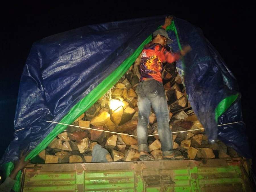 Worker loading firewood onto truck at night