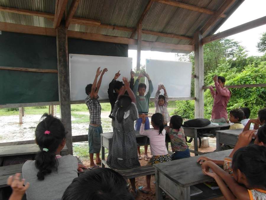 Students raising hands eagerly in open-air classroom