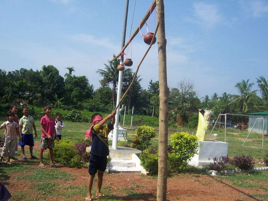Blindfolded child hitting clay pot on stick at school celebration