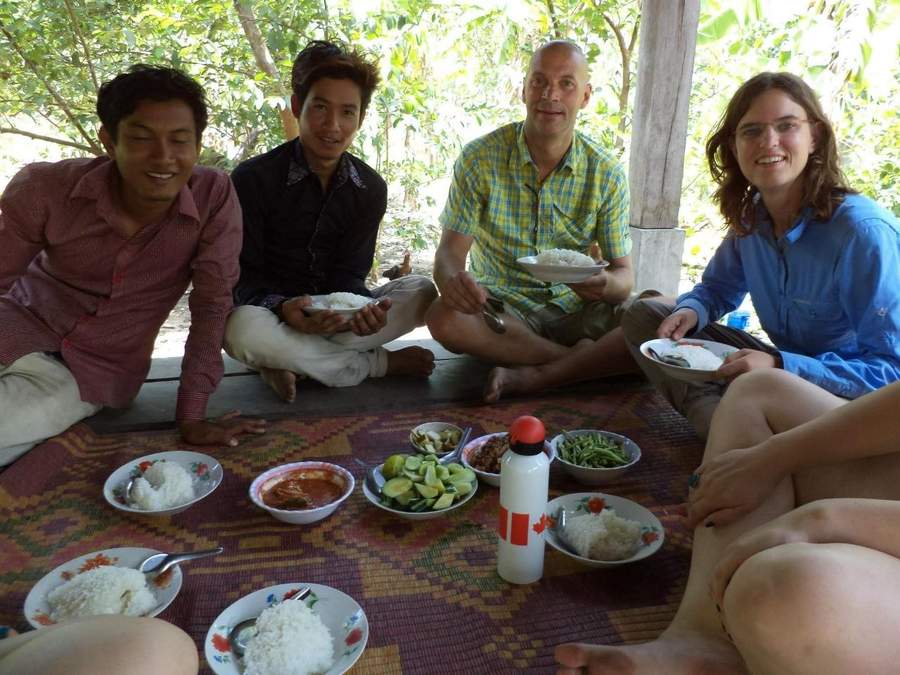 Four people sitting on mat sharing rice meal with local dishes