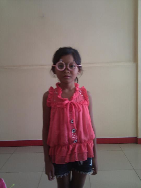 Young girl with pink glasses standing against wall