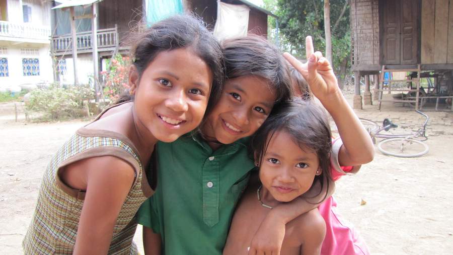 Three young girls hugging and smiling in village setting