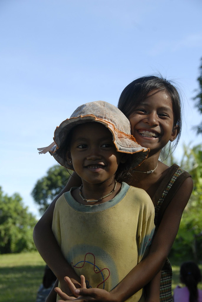 Two girls hugging and smiling outdoors with blue sky