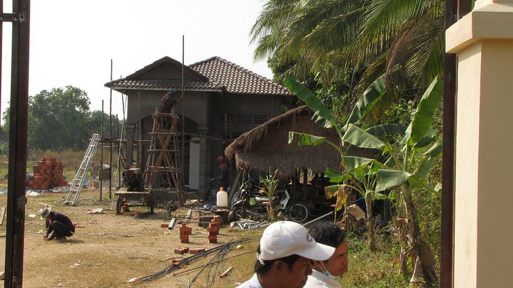 Building under construction with thatched-roof shelter and palm trees