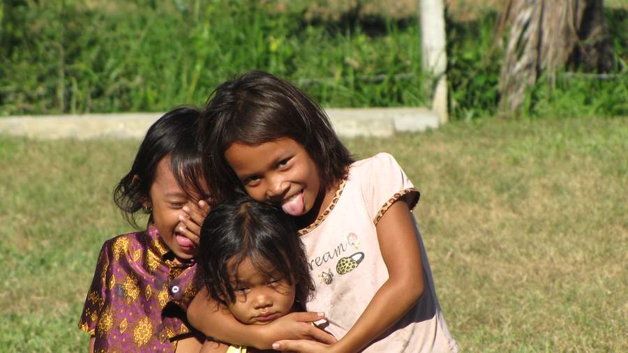 Three girls hugging and making funny faces in grassy field