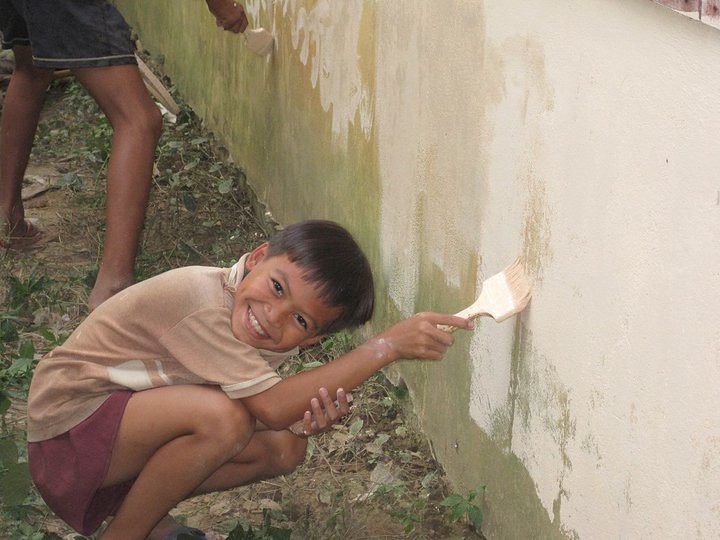 Young boy crouching and painting wall with brush smiling