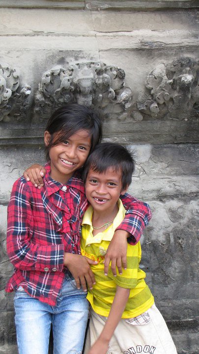 Two children hugging and smiling against ornate stone wall