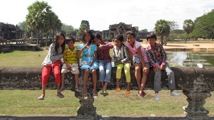 Group of children sitting on stone ledge at Angkor Wat temple
