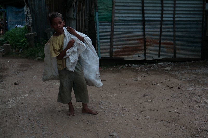 Boy carrying white sack on dirt road in village