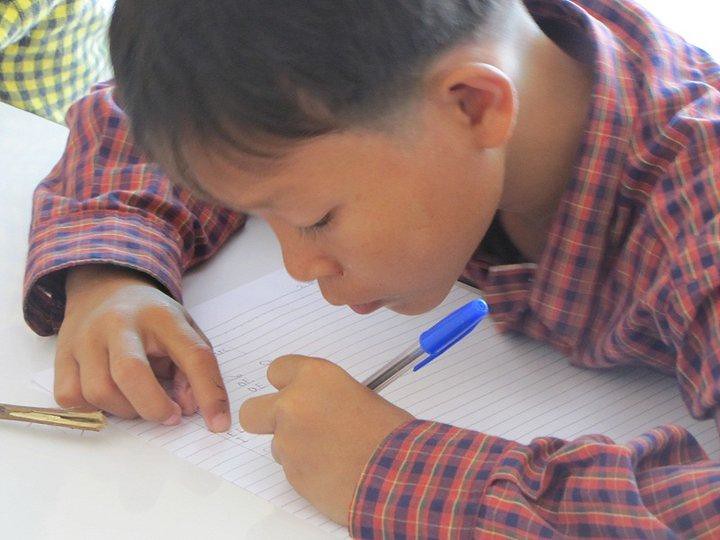 Young boy focused writing in notebook with blue pen