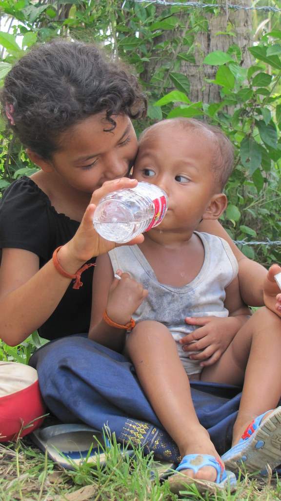 Girl giving water to toddler sitting on grass
