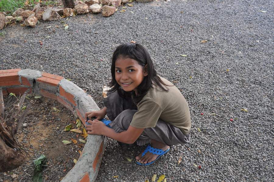 Young girl crouching by brick garden border smiling