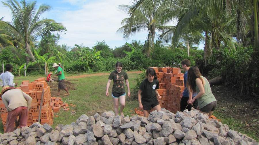 Volunteers carrying rocks and bricks at construction site with palm trees