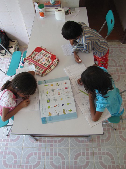 Three children studying at table with notebooks and textbook