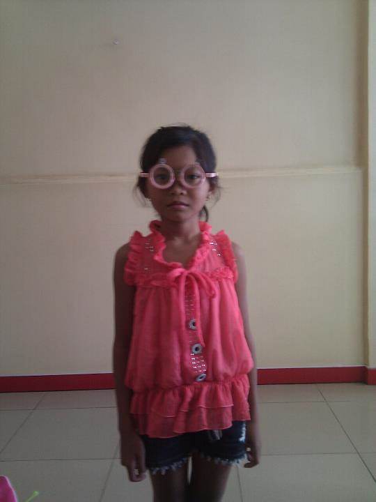 Young girl in pink shirt with pink glasses standing against wall
