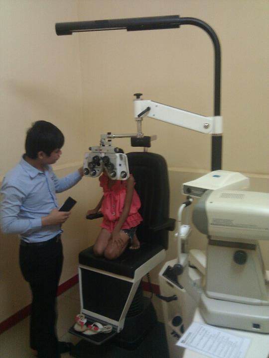 Eye exam young girl in pink shirt having eye tested with phoropter