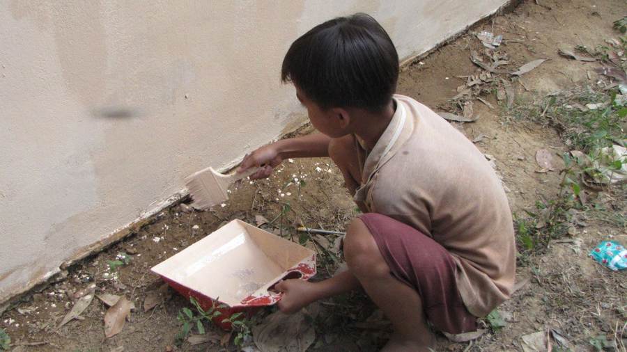 Young boy crouching and painting wall with brush and paint tray
