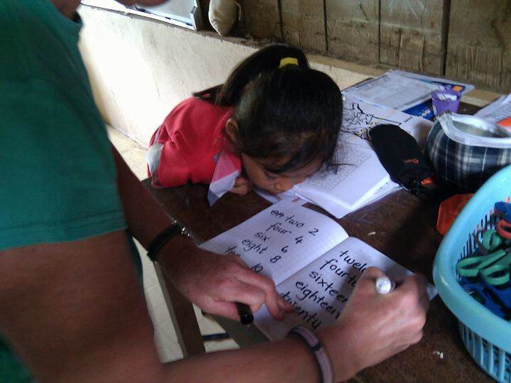 Volunteer teaching English numbers to young girl at desk