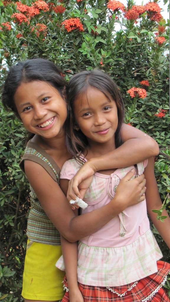 Two girls hugging in front of red flowering bush