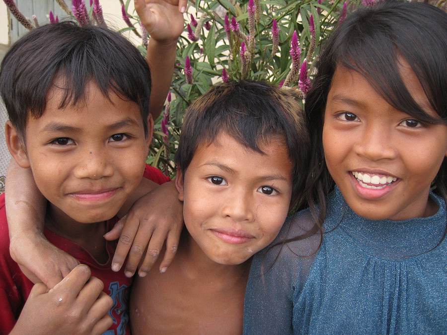 Three children smiling close-up with purple flowers