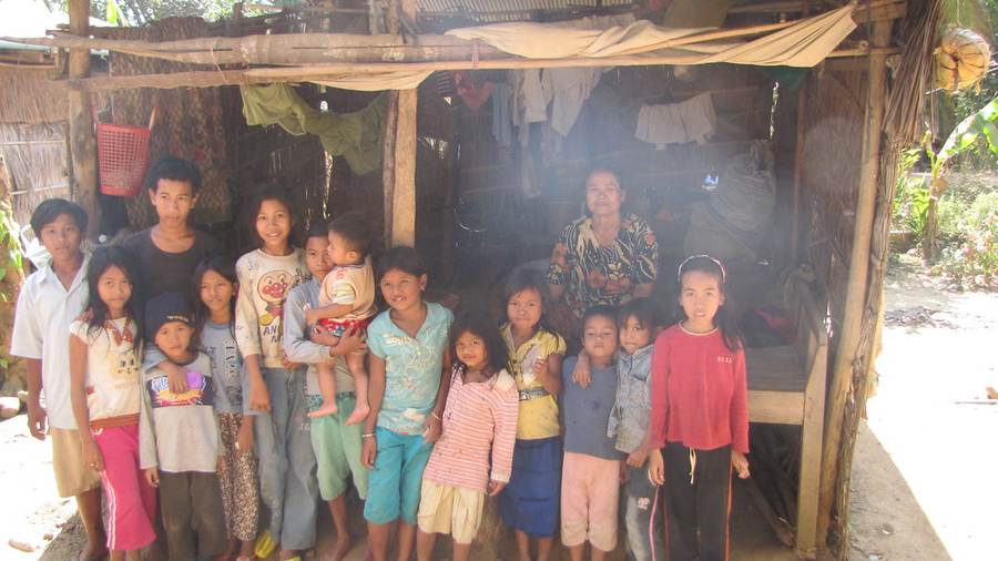 Large family group standing in front of thatched-roof home