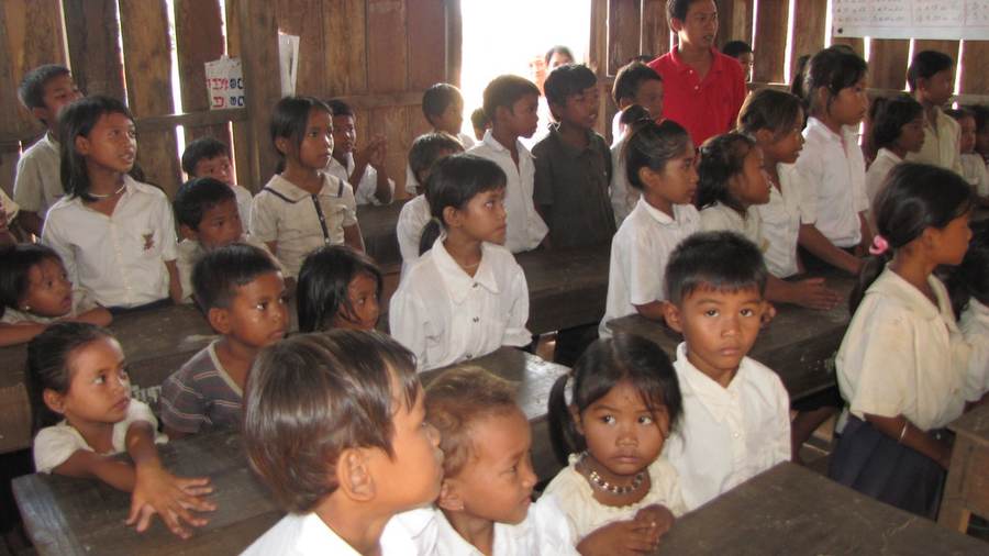 Students in white shirts seated in wooden classroom