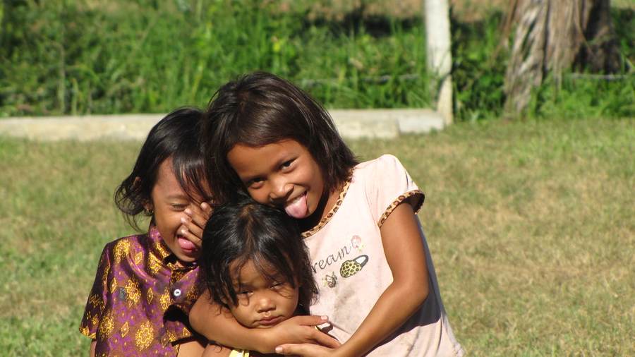 Three children hugging and playing on grass