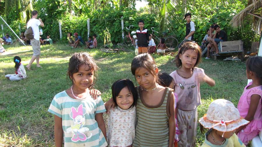 Group of children posing together at outdoor gathering with thatched-roof structure