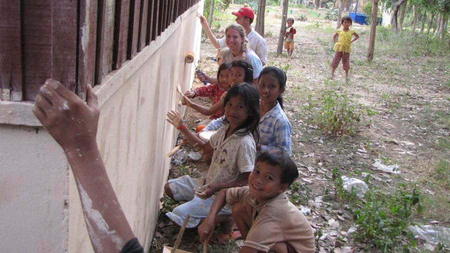Volunteers and children painting school building wall