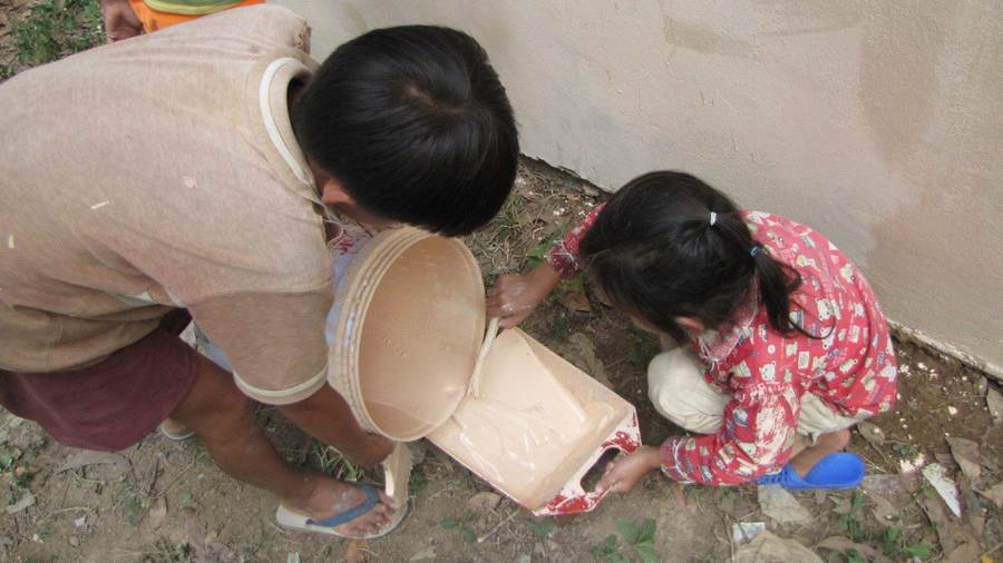 Two children pouring paint from bucket into tray
