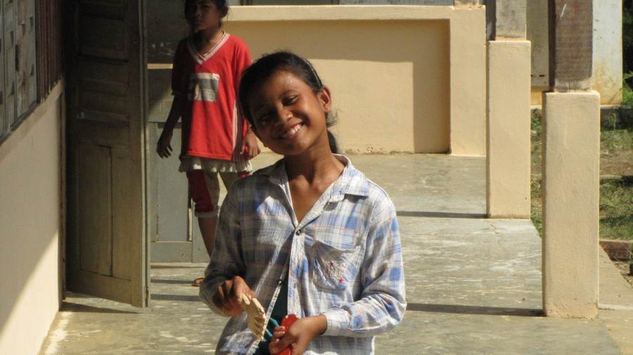 Girl in plaid shirt smiling holding paint brush on porch
