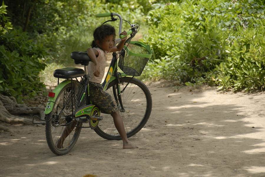 Girl sitting on bicycle on dirt path with green basket