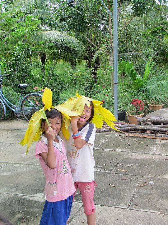 Two girls playing with large yellow leaves as hats in courtyard