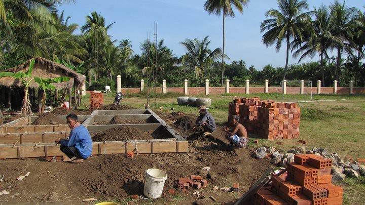 Workers at construction site laying foundation with brick piles