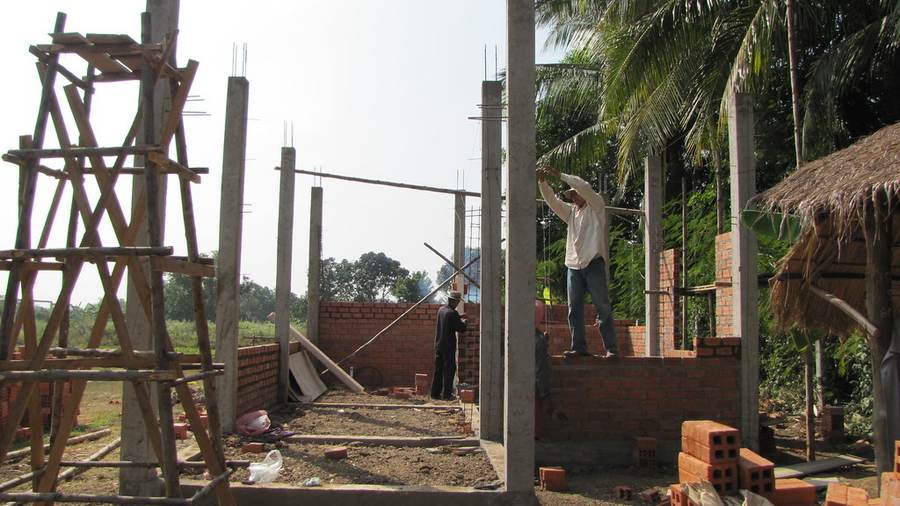 Workers building brick walls with concrete pillars at construction site
