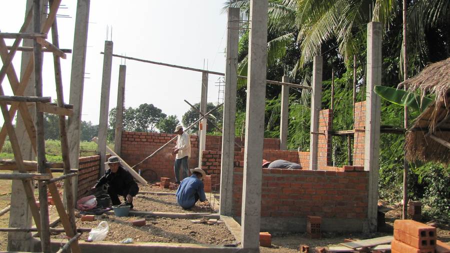 Workers at construction site with brick walls and bamboo scaffolding