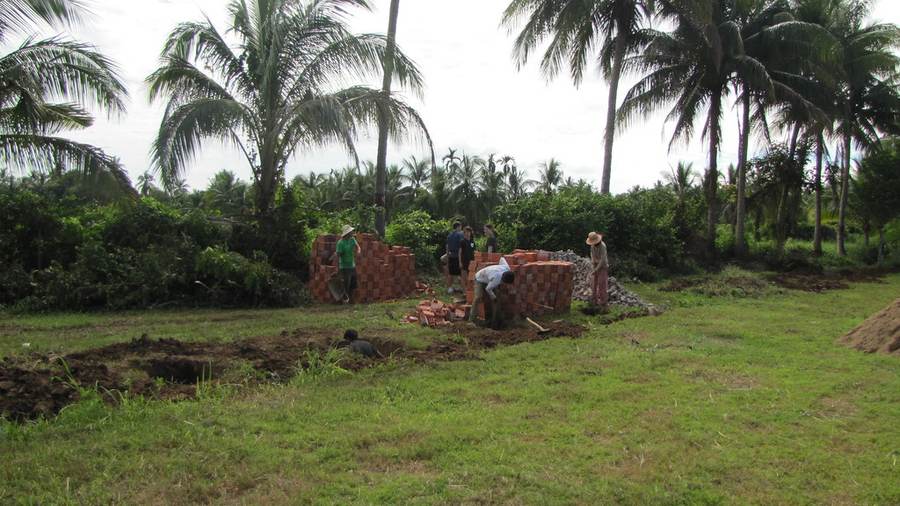 Workers moving bricks at construction site with palm trees