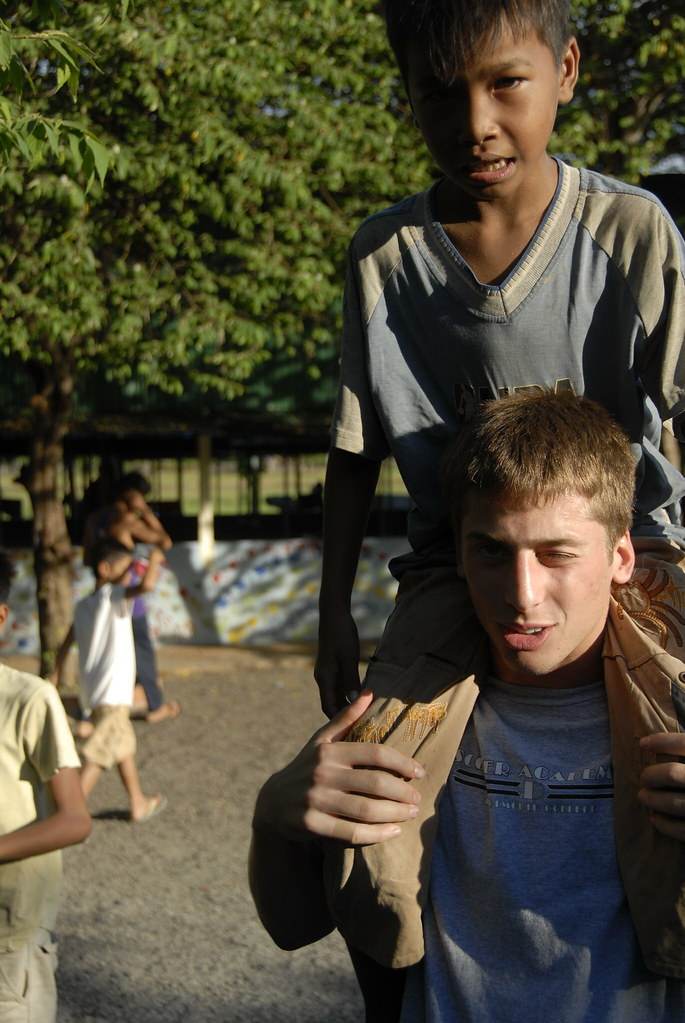 Young man carrying Cambodian boy on shoulders at playground