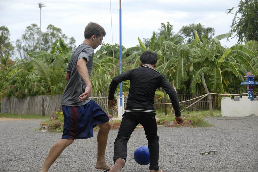 Volunteer playing soccer with Cambodian child on gravel field